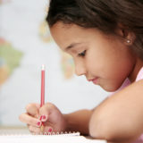 Junges Mädchen mit Stift in der Hand, schreibt etwas auf einen Block.