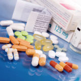 Medikamentenverpackungen und Beipackzettel, vor denen eine Auswahl an Tabletten in verschiedenen Größen und Formen liegt