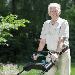 lächelnder Rentner der im Garten den Rasen mäht, Rasenmäher