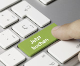 Ein Finger drückt auf eine grüne Taste einer Tastatur mit der Aufschrift "Jetzt buchen".