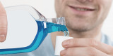 Mann schüttet blaue Mundspüllösung in einen Dosierbecher