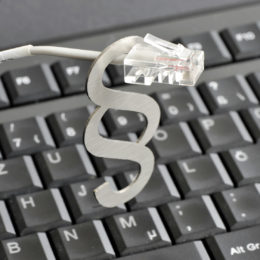Ein LAN-Kabel steckt in einem silbernen Paragraphenzeichen auf einer schwarzen Tastatur.