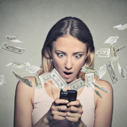 Frau guckt geschockt auf ihr Smartphone, während Geldscheine durch die Luft flattern