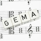 weiße Würfel mit der Aufschrift GEMA auf Musiknoten