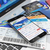 Handy, Kreditkarte und Flugtickets liegen auf einem Laptop, Flüge online Online buchen