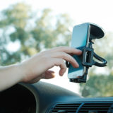 Smartphone hängt in einer Saugnapfhalterung an der Windschutzscheibe eines Autos und wird von einer Hand bedient