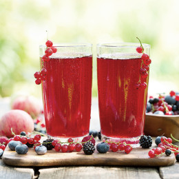 zwei Gläser mit rotem Saft die auf einem Holztische mit verschiedenen Beeren stehen