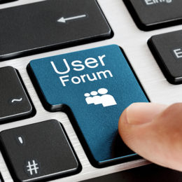 Ein Finger drückt auf eine blaue Taste einer schwarzen Tastatur mit der Aufschrift "User Forum".