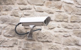 Weiße Überwachungskamera an einer steinernen Hauswand.