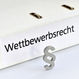 ein weißer ordner mit der Aufschrift "Wettbewerbsrecht" liegt auf dem Tisch, ein Paragrafenzeichen steht davor