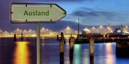 Wegweiser mit der Aufschrift "Ausland" vor einer sich im Wasser spigelnden Stadt