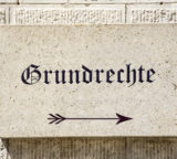 Steintafel an einer Hauswand auf der "Grundrechte" steht, darunter ein Pfeil nach rechts