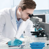Mann in weißem Laborkittel schaut in einem Labor in ein Mikroskop