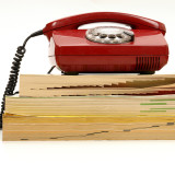 rotes Telefon mit Wählscheibe auf einem Stapel Telefonbücher