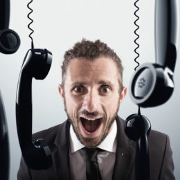 Telefonhörer, die von der Decke hängen, dahinter wütender Mann