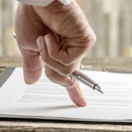 Männerhand, die einen Stift hält und mit dem Zeigefinger auf ein Dokument deutet