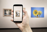 Mann hält ein Smartphone in einem Museum und fotografiert ein Gemälde