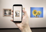 Mann hält ein Smartphone in einem Museum und fotografiert ein Gemälde