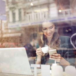 Frau in Cafe nutzt mit Handy und Laptop WiFi