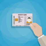 Hand hält einen Personalausweis vor blauem Hintergrund