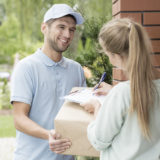 Ein Postbote bringt ein Paket, die Empfängerin unterschreibt