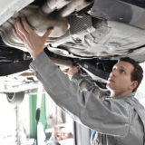 Automechaniker in einer Autowerkstatt kontrolliert Abgasanlage