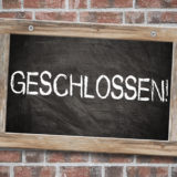 Schild mit weißem Schriftzug "GESCHLOSSEN" vor roter Ziegel-Wand