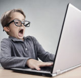 Kind sitzt vor dem Laptop mit entsetztem Gesichtsausdruck