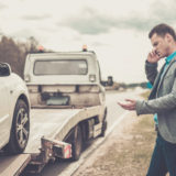 junger Mann telefoniert während ein Abschleppwagen sein Auto auflädt