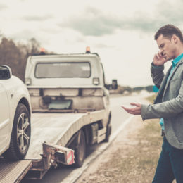 junger Mann telefoniert während ein Abschleppwagen sein Auto auflädt