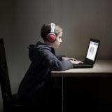 Kind sitzt mit Kopfhörern vor einem Laptop an einem Tisch