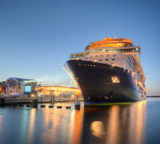 großes Kreuzfahrtschiff, das bereits beleuchtet ist und während der Dämmerung im Hafen liegt