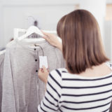 eine Frau betrachtet in einem Bekleidungsgeschäft das Preisschild eines grauen Shirts