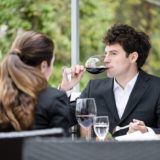 Ein Mann und eine Frau sitzen gemeinsam beim Essen. Der Mann trinkt gerade Rotwein.