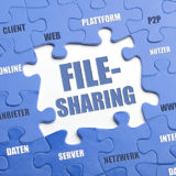 Das Wort "Filesharing" zentral in einem Puzzle aus blauen Puzzleteilen mit Aufschriften wie "Server", "Daten", "Anbieter", "Online", "Web", "Plattform", "Client", "Nutzer"