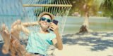 Urlauberin mit Handy in der Hand in der Hängematte am Strand