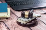 Richterhammer, unter dem Geld liegt sowie Laptop und Akten im Hintergrund