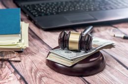 Richterhammer, unter dem Geld liegt sowie Laptop und Akten im Hintergrund