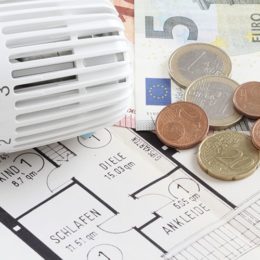 Thermostat liegt auf Grundriss neben Euromünzen