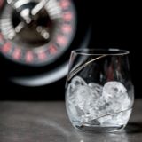 Whiskyglas mit Eiswürfeln steht auf einem Tisch, im Hintergrund die Oberseite eines Roulettekessels