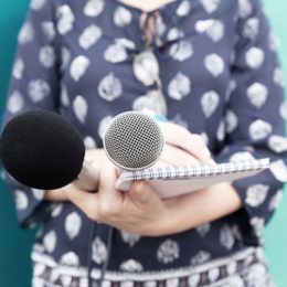 weibliche Journalistin mit zwei Mikrofonen, Zettel und Stift
