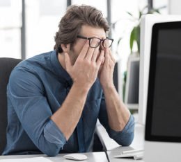 Mann am Schreibtisch reibt sich Augen