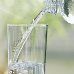 Wasser wird aus einer Wasserflasche in ein Glas eingeschenkt