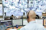 Mann sitzt in einem Überwachungsraum mit vielen Monitoren