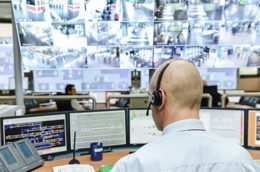 Mann sitzt in einem Überwachungsraum mit vielen Monitoren