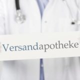 Schild mit Aufschrift Versandapotheke vor Apotheker-Kittel