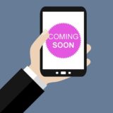 Hand hält Smartphone, auf dem ein Button mit der Aufschrift "Coming Soon" zu sehen ist