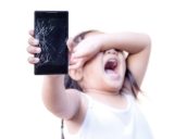Baby schreit und hält ein Smartphone mit einem kaputten Display vor sich
