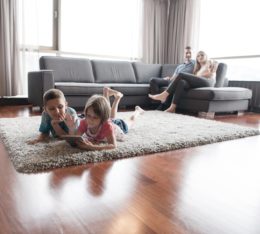 Pärchen sitzt auf dem Sofa und beobachtet Kinder, die im VOrdergrund mit einem Tablet auf dem Teppich liegen