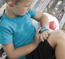Kind sitz mit einer Smartwatch am Handgelenk auf einer Bank